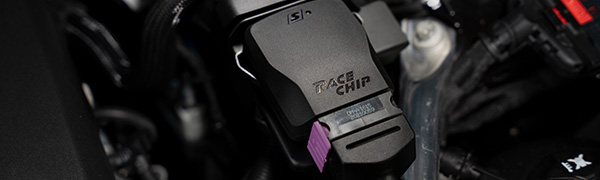 Close-up van de RaceChip S-besturingseenheid in een motorruimte, zwarte behuizing met RaceChip-logo, productlabel en paarse seriestekker.